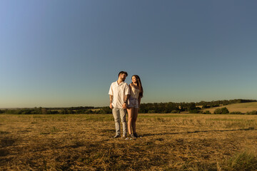 Beautiful couple hugging and kissing in a field at sunset