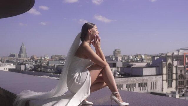 The bride sits on the parapet at the edge of a skyscraper