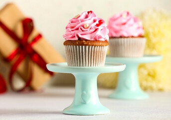 Stand with tasty cupcake for Valentine's Day on light background