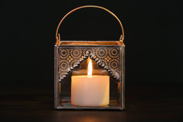 Silver Muslim lamp with burning candle for Ramadan on table against dark background