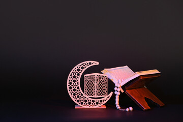 Rehal with Koran, prayer beads and decorative crescent for Ramadan on dark background