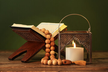 Silver Muslim lamp, rehal with Koran and prayer beads for Ramadan on wooden table against dark green background