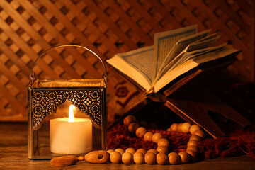 Silver Muslim lamp with burning candle, Koran and prayer beads Ramadan on wooden table, closeup
