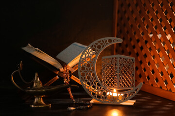 Decorative crescent, Koran and Aladdin lamp for Ramadan on table against dark background