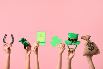 Female hands holding greeting card and party decor for St. Patrick's Day celebration on pink background