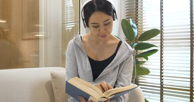 Young asian woman reading book on cozy couch sofa at warm home. Relax woman holding book read on sofa near window happiness.woman reading open book leisure mind. Happiness woman lifestyle at home