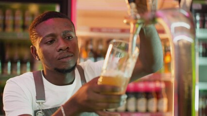 Barman pours ale into glass in bar closeup. Attentive African American bartender fills mug with craft beer from pump in club. Brewer serves beverage - Powered by Adobe