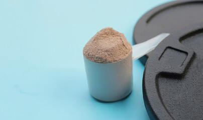 Whey protein powder with black weight plates on blue background.