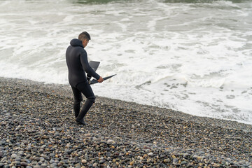 Fisherman in wetsuit holding flippers in front of the sea