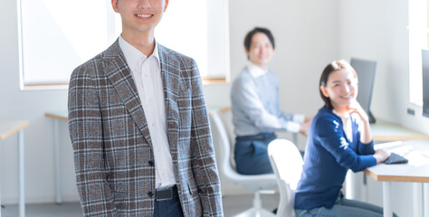 オフィスにいるカメラ目線のジャケットを着た若い日本人男性 - obrazy, fototapety, plakaty