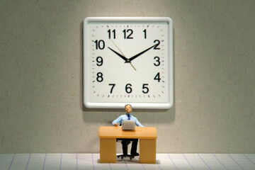 Miniature tiny people toy figure photography. Overload and work overtime concept. A businessman seat on a desk with big clock behind