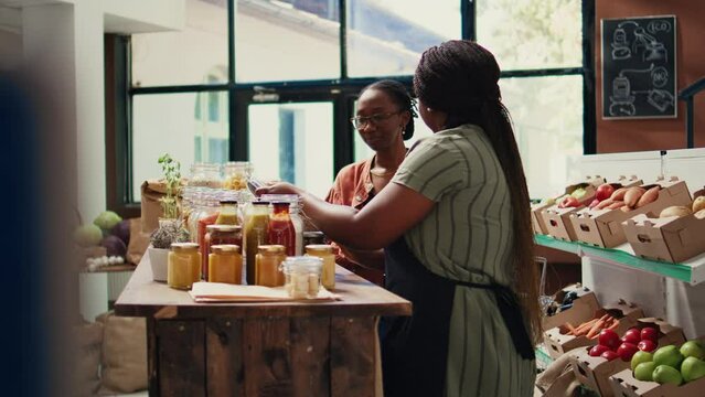 African american vendor giving food sample to shopper, recommending homemade snacks with organic ingredients. Vegan client trying out grocery store products before buying. Handheld shot.
