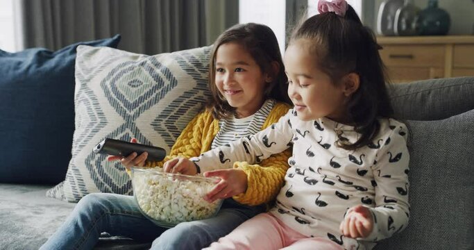 Watching tv, eating popcorn and funny children together in living room at family home. Television, food snack and girls laugh on sofa for comedy movie, show or happy sisters streaming cartoon video