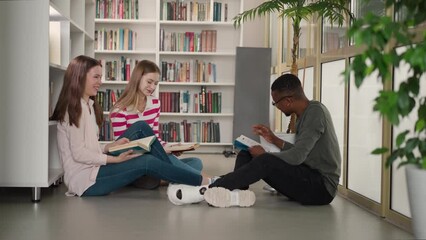 Happy students enjoy humorous book reading in library. Black man flirts with pretty women during reader club meeting in bookshop. Intellectual leisure