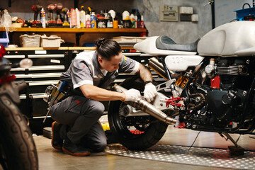 Mechanic in uniform concentrated on diagnosing and fixing common problems with motorcycle