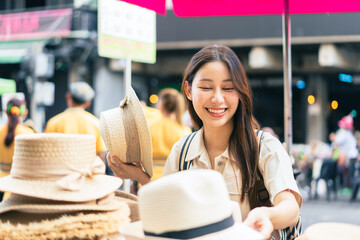 Young Asian woman traveler tourist shopping for a hat and walking at outdoor market in Bangkok in Thailand. People traveling, summer vacation and tourism - 716222805