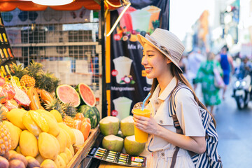 Young Asian woman traveler tourist buying a freshly made juice and walking at outdoor market in...