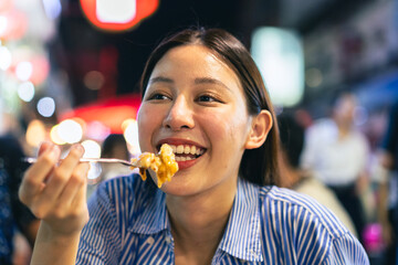 Young Asian woman traveler tourist eating Thai street food in China town night market in Bangkok in...