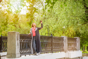 Fototapeta premium A cheerful woman poses behind the fence of a small bridge. A walk in the city park
