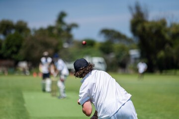a local cricket match being played on a green cricket oval in summer in australia. australian cricketer batting and bowling in a game
