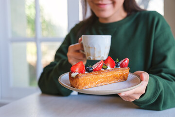 Closeup image of a woman holding a plate of mix berry log croissant and coffee cup