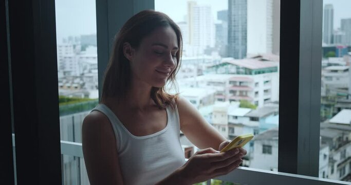 Woman sits on windowsill looking out window smiling communication with friends close-up. Communication with friends amidst home's warmth Communication with friends enjoying friendship.