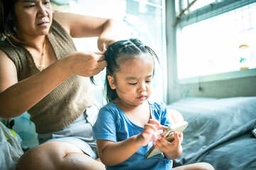 Fototapeta premium Daughter play smartphone while mom hair dress in cozy room