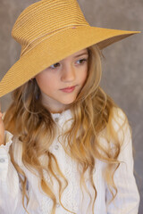 portrait of a beautiful long-haired blonde girl in a white blouse and a straw hat on a gray background