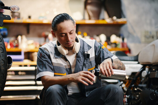 Mechanic pouring himself cup of coffee from thermos when having lunch break