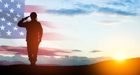 Silhouette of soldier saluting on background of sunset or sunrise and USA flag. Greeting card for...