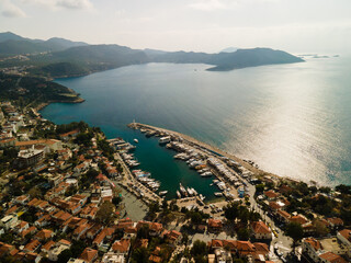 The coast is a dark turquoise sea and the gulf of the Mediterranean Sea at sunset. Beautiful houses on the shore, beach, harbor, mountains and sky. Aerial view from a drone. Antalya, TURKEY.