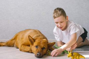 Cute boy sits near his dog at home and plays with toys