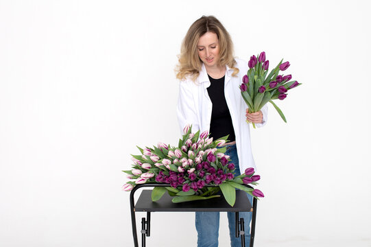 Cute florist girl in a shirt takes a purple and white tulip from the table for a birthday gift