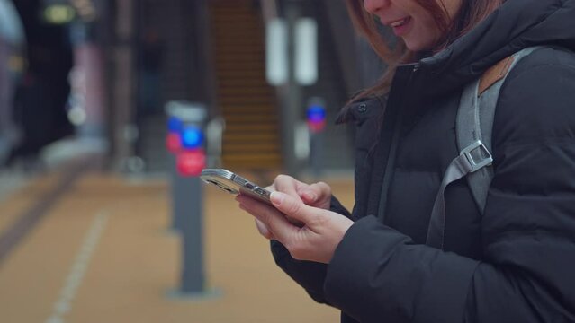 Closeup - Happy woman using smart phone while waiting on station platform, Female using mobile phone at train station, Enjoying travel concept