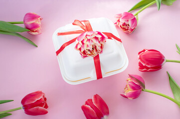 Colorful red double tulips lie around a white gift box with a red ribbon. View from above