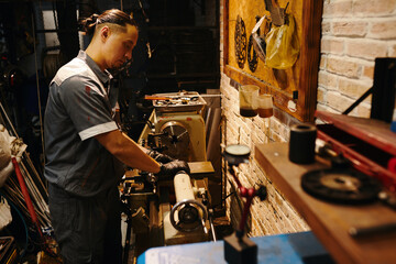 Mechanic using special machine at workbench to fix detail for motorcycle - obrazy, fototapety, plakaty