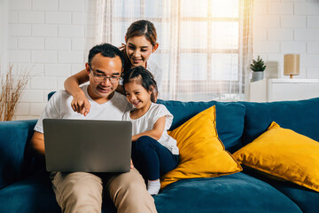 In their cozy home parents and children gather on the couch with a laptop connecting through modern...