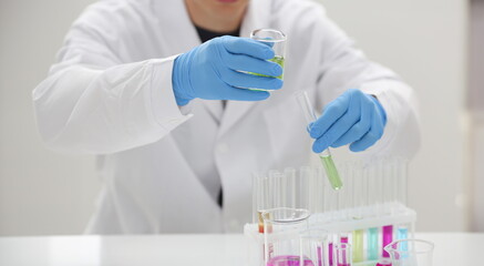 Fototapeta premium A male chemist holds test tube of glass in his hand overflows a liquid solution of potassium permanganate conducts an analysis reaction takes various versions of reagents using chemical manufacturing.