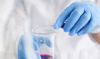 A male chemist holds test tube of glass in his hand overflows a liquid solution of potassium permanganate conducts an analysis reaction takes various versions of reagents using chemical manufacturing.