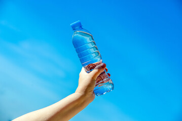A girl holds a bottle of drinking water in her hand against a blue sky background
