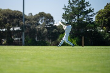 cricketer batting on a cricket pitch, a local cricket match being played on a green cricket oval in summer in australia - obrazy, fototapety, plakaty