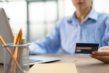 Woman using credit card and laptop in the office.
