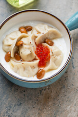 Vareniki dumplings served with yogurt and red caviar in a turquoise pan, vertical shot on a beige granite surface, middle close-up