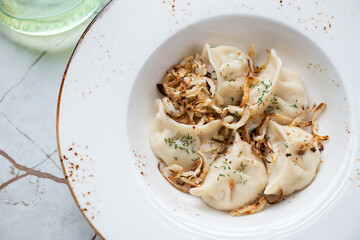 Closeup of vareniki or stuffed dumplings served with roasted onion in a beige plate, horizontal shot, selective focus, elevated view