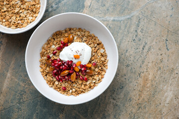Granola bowls with yogurt, pomegranate seeds and nuts, top view on a beige and grey granite background, horizontal shot with space