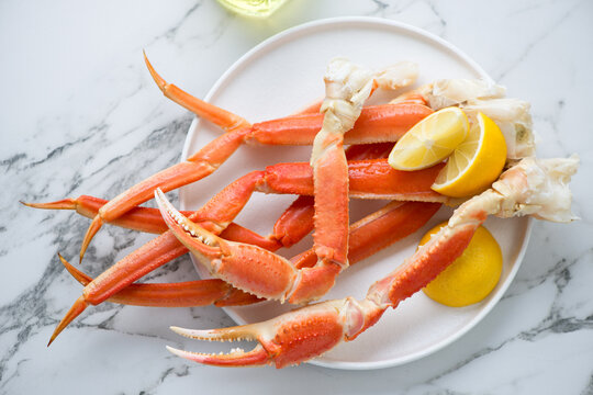 Plate with boiled crab claws and legs on a white marble background, horizontal shot, above view