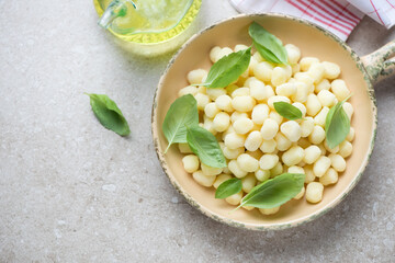 Serving pan with uncooked potato gnocchi and green basil leaves, horizontal shot on a beige stone background with space, high angle view