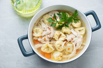 Serving pan with tortellini and chicken soup on a light-grey granite background, horizontal shot