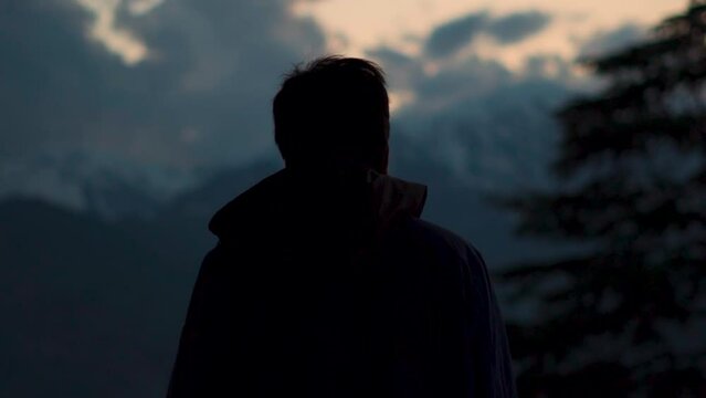 Silhouette shot of an Indian man staring at the snow covered mountains during the sunset at Manali in Himachal Pradesh, India. Man staring at the beautiful mountain peaks during sunset.
