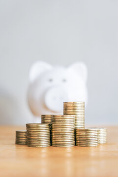 Upward financial growth stack of golden money coin on wooden table and white piggy bank in the background. Financial and saving money concept background. 